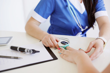 Female doctor with otoscope and pulse oximeter in blue uniform making oxygen test to a patient. Medicine and health care concept. - obrazy, fototapety, plakaty