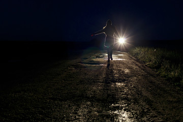 running scared woman at night in the headlights of a car on a country road silhouette