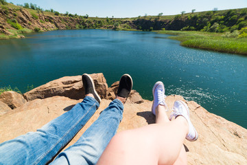 Travelers couple in sports shoes on a mountain near a river in the background of nature. Man and woman. A couple sits and makes their feet on a beautiful landscape with a river bank summer