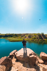Fototapeta premium guy tourist on a cliff face looking at a pond, tourism, vacation, travel, summer vacation
