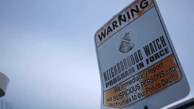 Camera pans to a dramatic neighborhood watch program sign