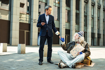 Elderly homeless. White collar worker giving his big meat burger to elderly homeless man sitting on the floor