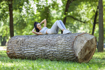 Young fit beautiful girl doing sit ups on a tree log