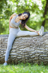 Young fit beautiful girl resting and stretching on a tree log