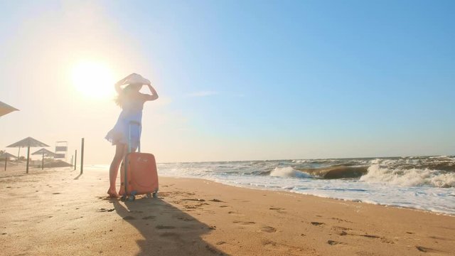 Young woman with a suitcase sitting on the beach. a young girl walks along the beach with a wheeled suitcase.Shags along the sand along the sea. The girl is looking for herself and adventure