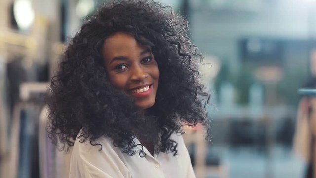 Portrait of fashionable young african american woman look at camera at clothing store smile design girl face beautiful buying attractive shop cute black happy pretty style curly hair slow motion