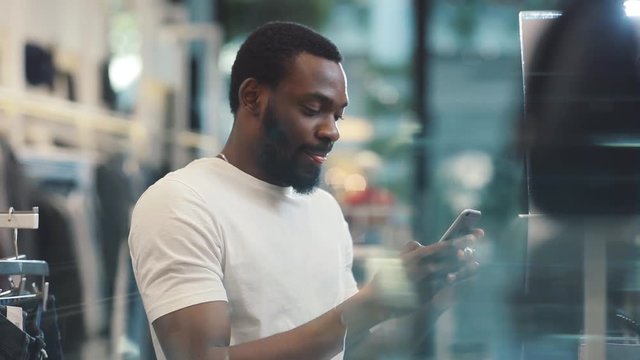 Portrait young african american man using phone texting message stand at clothes store look at camera smile internet happy black telephone cute mobile holding slow motion portrait close up