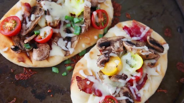 A woman adds chopped scallions to naan bread pizzas and cuts one into portions