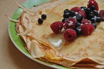 thin pancakes with raspberries, blueberries and condensed milk on a plate