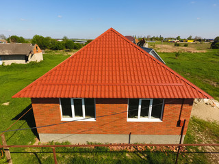 Fototapeta premium House with an orange roof made of metal, top view. Metallic profile painted corrugated on the roof