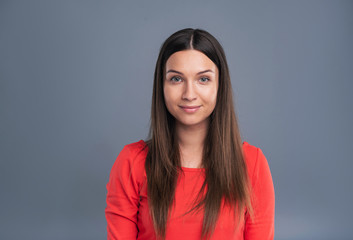 Fototapeta premium Attractive woman. The portrait of a beautiful dark-haired woman in a red blouse smiling at the camera while posing isolated on a blue-grey background