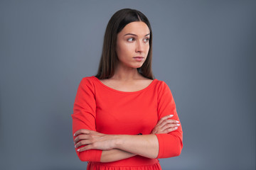 Fototapeta premium Refined beauty. The portrait of a beautiful young woman in a red dress crossing her arms and posing for the camera while standing isolated on a blue-grey background
