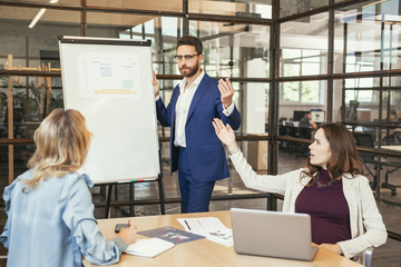 Obraz premium Team brainstorm. Sincere female colleagues staring at whiteboard and man standing near whiteboard