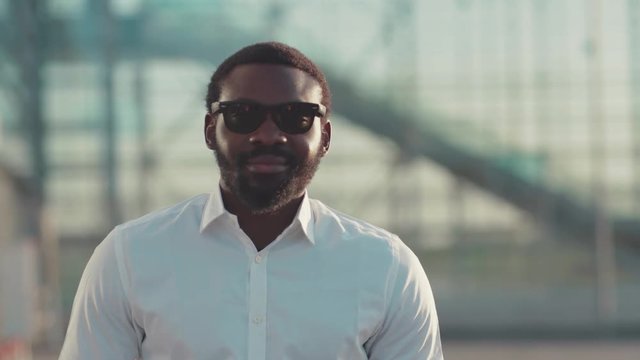 Young attractive bearded Afro-American man in sunglasses, in formal wear looks straight to camera seductively smiling. Having fun, confident, male power. Male portrait