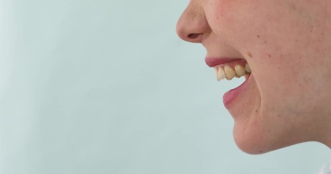Close up of woman smiles and laughs or screams with her mouth open side view on a blue background