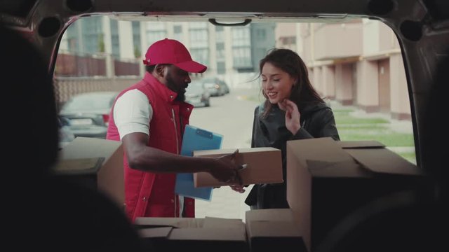 Portrait courier African American gives a parce to a woman after signing on delivery device cardboard technology box order post postal service device sunny beard covered load logistic mailman