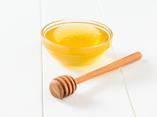 A bowl of honey and a wooden honey spoon on a white wooden table.