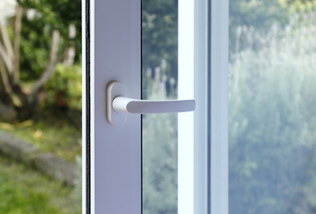 Open door of a family home. Close-up of the lock on the sliding door with the yard of background. White PVC door and double glass.