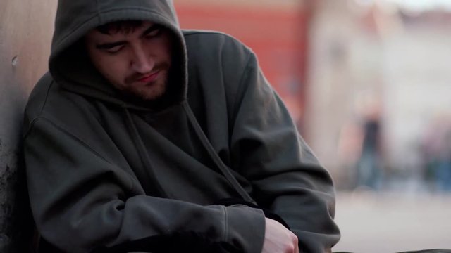Close up homeless man sitting on street with sign people walk around honeliness sad social cardboard homeless beggar face poverty poor hungry dirty unemployed despair male slow motion portrait