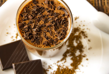 a glass of mousse dessert with chocolate chips on a white plate