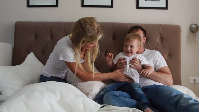 Loving parents play with their son on the bed laughing and smiling in the bedroom