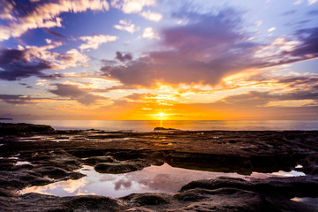 Beachside sunrise on a cloudy morning, a serene landscape for a lonely dawn with a pool of reflections in the rocky foreground.