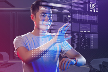 Using a smart watch. Positive emotional programmer feeling impressed and putting his hand up while using a modern smart watch for creating holograms