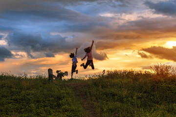 Fototapeta na wymiar Silhouettes of happy two children play jumping on mountain at sunset time