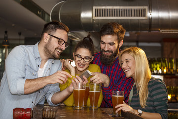 Goup of four friend in local pub looking at mobile phone and smile with glass of beer on hands