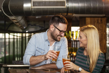 Young couple looking each other in local pub with glass of beer