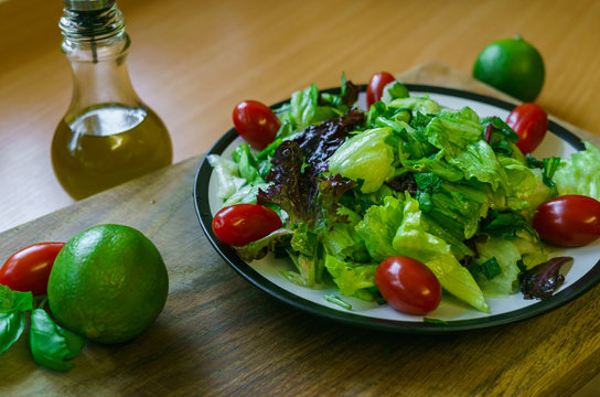 Fresh salad from different types of greens and cherry tomatoes, seasoned with olive oil and lime juice with lemon