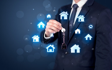 Businessman in suit holding keys with house graphics around and dark background
