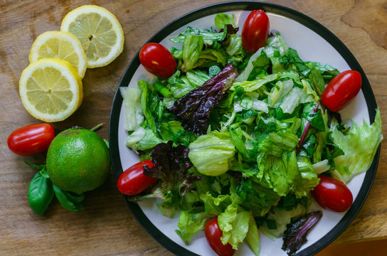 Fresh salad from different types of greens and cherry tomatoes, seasoned with olive oil and lime juice with lemon