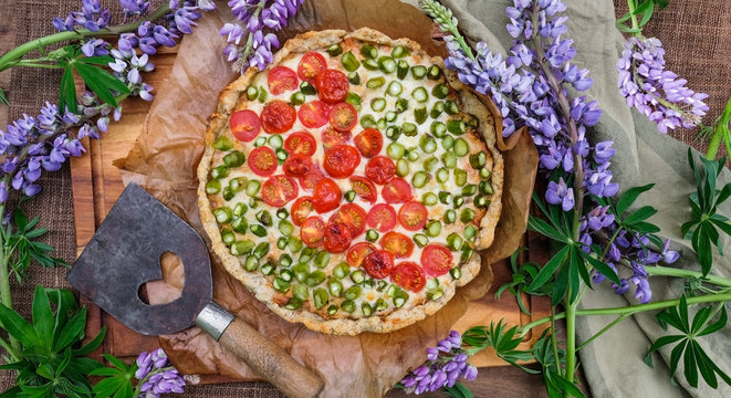 Aspargus cherry tomato pie on the table for summer festivites. Decorated with blue lupines. Flat lay and top view for quice