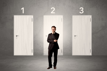 Businessman in grey room with three numbered white  door behind his back
