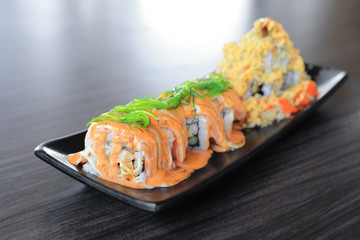 Maki sushi roll made of salmon top with wakame seaweed and special sushi top with crispy tempura flour, mayonnaise and flying fish roe - Japanese fusion