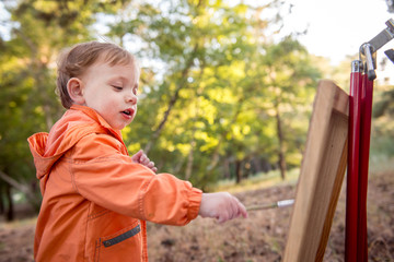 Boy draws on the blackboard in summer. little boy is drawing. Young artist.  Funny boy is engaged in creativity in the park. Summer activity for children
