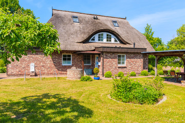 Fototapeta na wymiar SEEDORF VILLAGE, RUEGEN ISLAND - MAY 28, 2018: Garden with traditional thatched roof house near Seedorf village, Baltic Sea, Germany. Rugen is popular tourist destination due to its rural landscape.