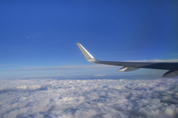 View from airplane window with silver wing, blue sky, white clouds and horizon; Flight above the clouds