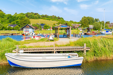 Fishing boats mooring in Baabe port and view of Moritzdorf village with houses on lake shore, Ruegen island, Baltic Sea, Germany