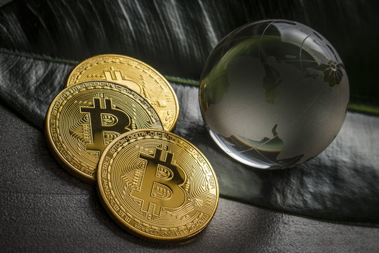 Three gold coins in the form of bitcoin on a table with a glass globe