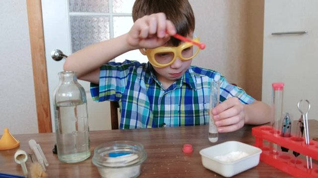 Experiments on chemistry at home. Chemical reaction with the release of gas in a test tube in the hands of a surprised boy.