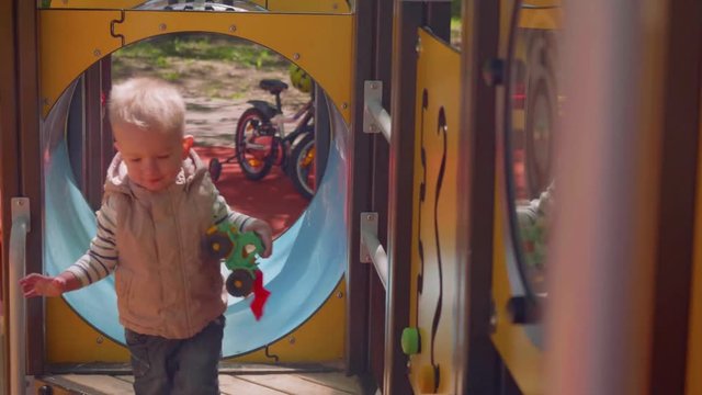 Little blond toddler approaches camera playing on playground