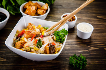 Roasted meat, rice noodles and vegetables on wooden background