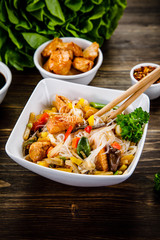 Roasted meat, rice noodles and vegetables on wooden background