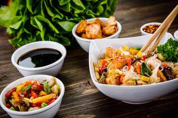 Roasted meat, rice noodles and vegetables on wooden background