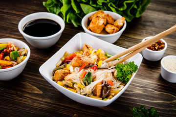 Roasted meat, rice noodles and vegetables on wooden background