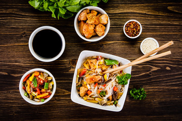 Roasted meat, rice noodles and vegetables on wooden background