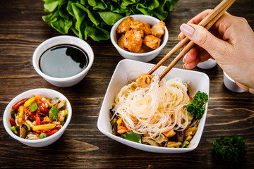 Roasted meat, rice noodles and vegetables on wooden background