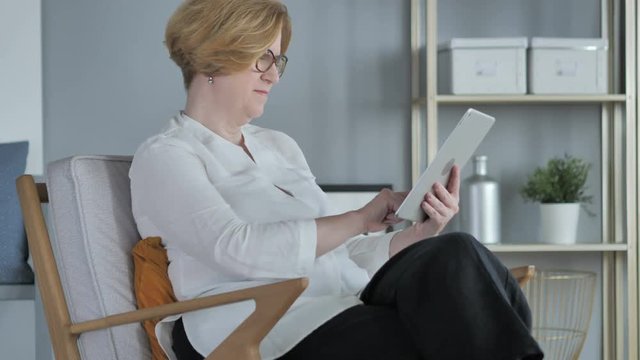 Old Senior Woman Browsing Internet on Tablet PC, Sitting on Couch